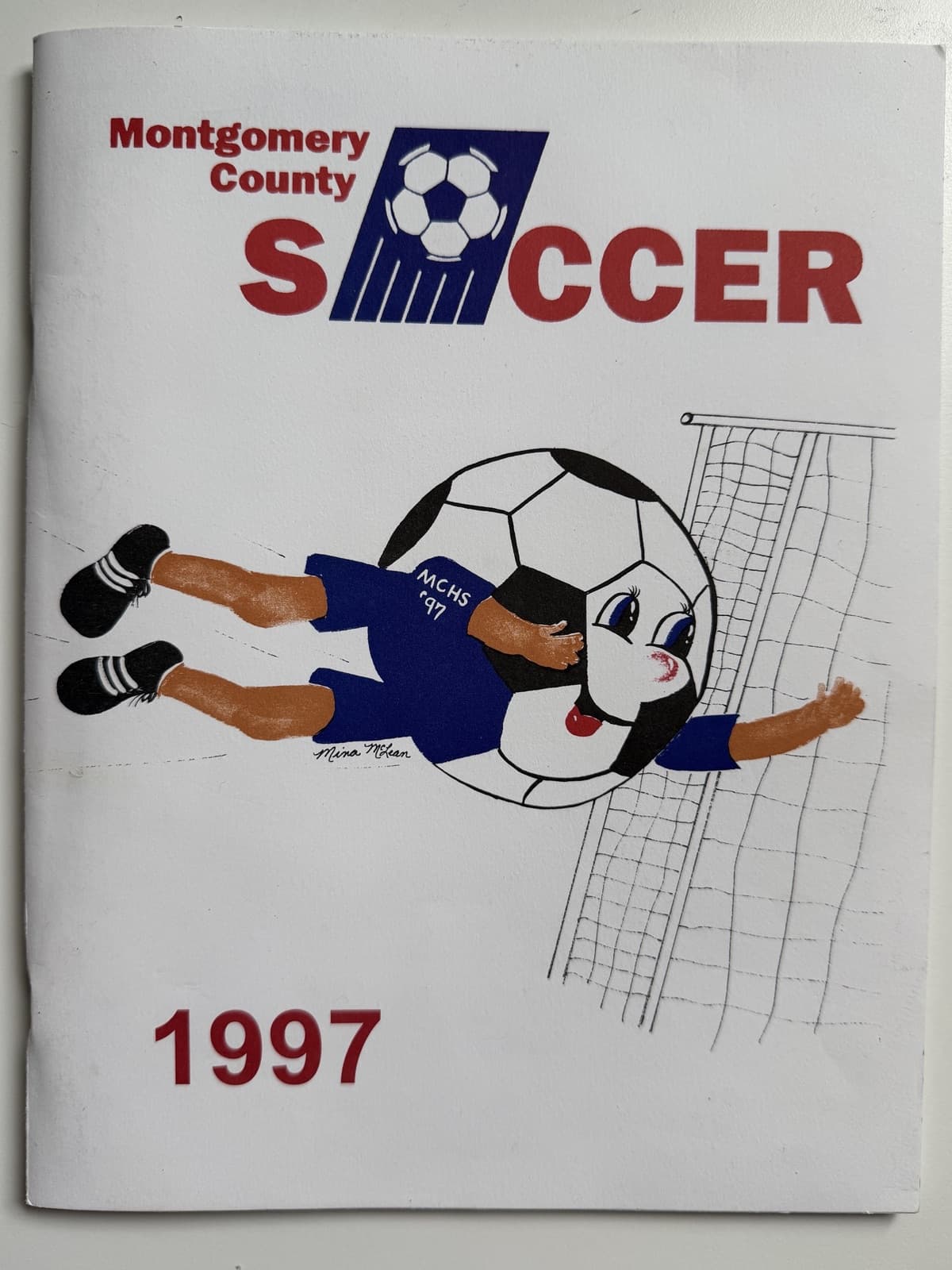 The hand-painted cover of the 1997 Montgomery County Soccer program: a cartoon player in an MCHS ’97 jersey whose head is a giant soccer ball, diving full-stretch at the goal, beneath the “Montgomery County SOCCER” wordmark and above a red “1997”